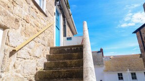 A stone staircase leading to a building with a blue door and a white sign. - Seagulls Nest (St Ives)