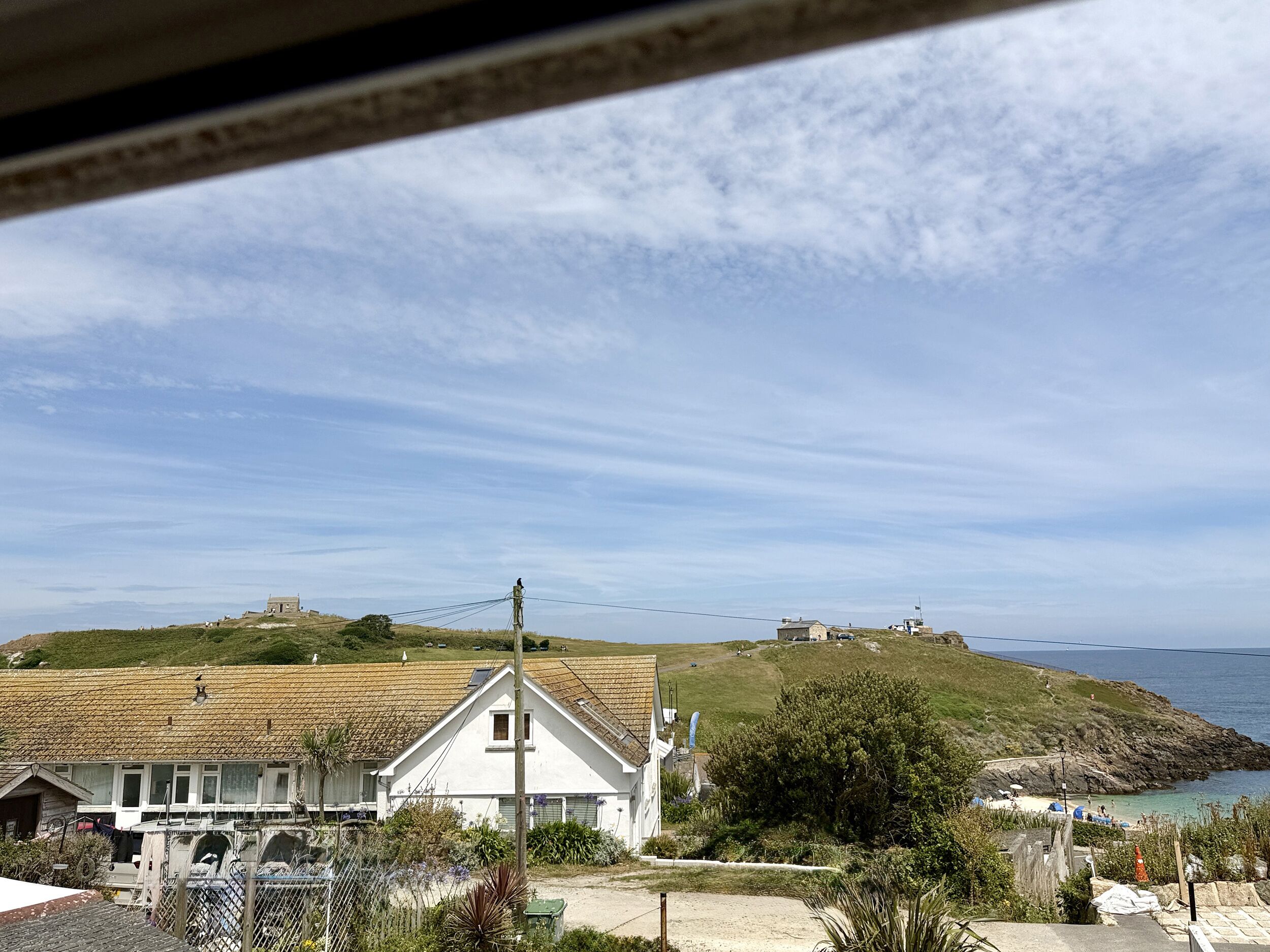 A coastal view with a white house, a hill with a structure, and a beach with umbrellas.