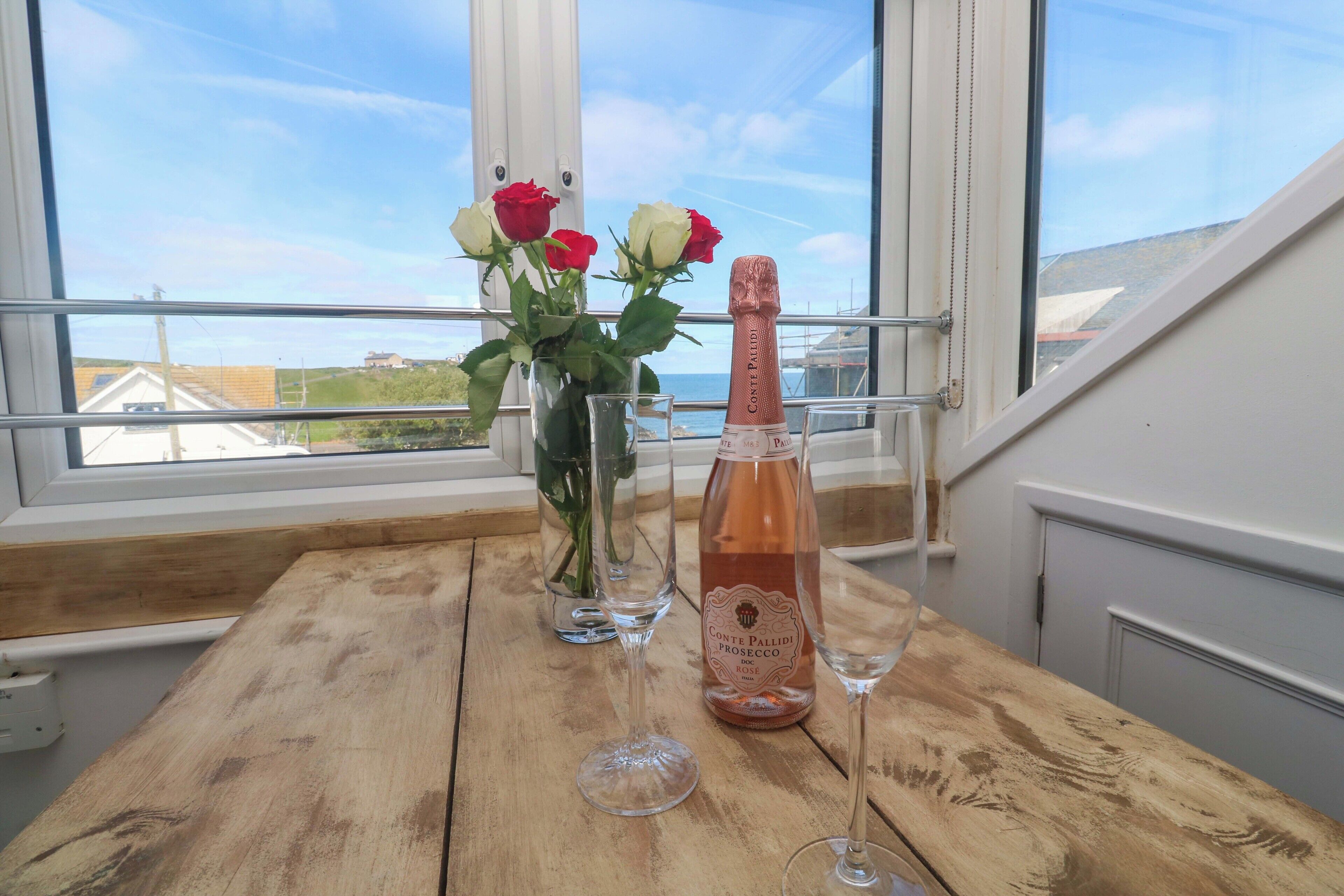 Ein Holztisch mit einer Flasche Conte Pallidi Prosecco, zwei Weingläsern und einer Vase mit roten und weißen Rosen.