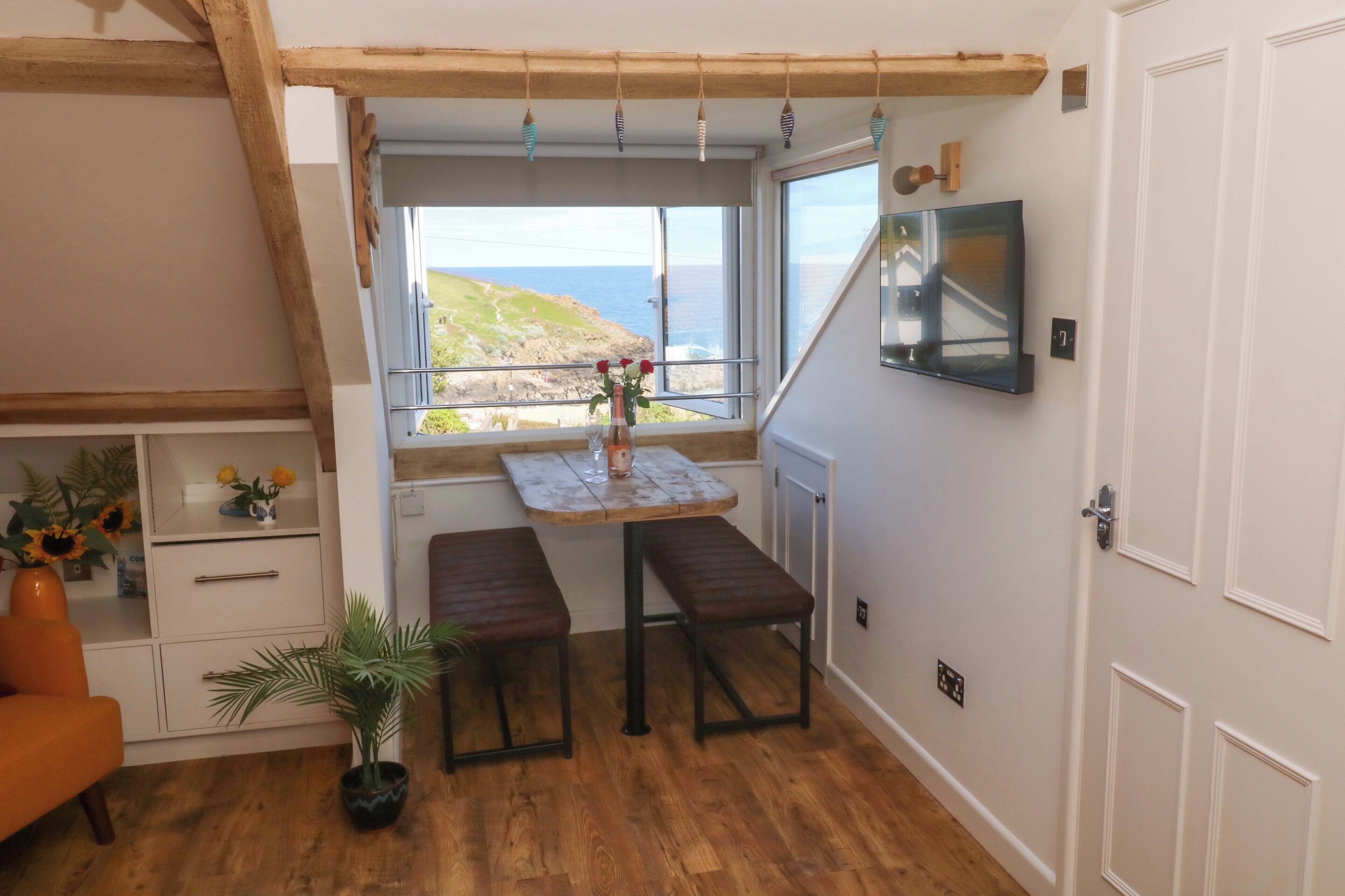 A room with a wooden bench, a small table, a potted plant, and a view of the sea.