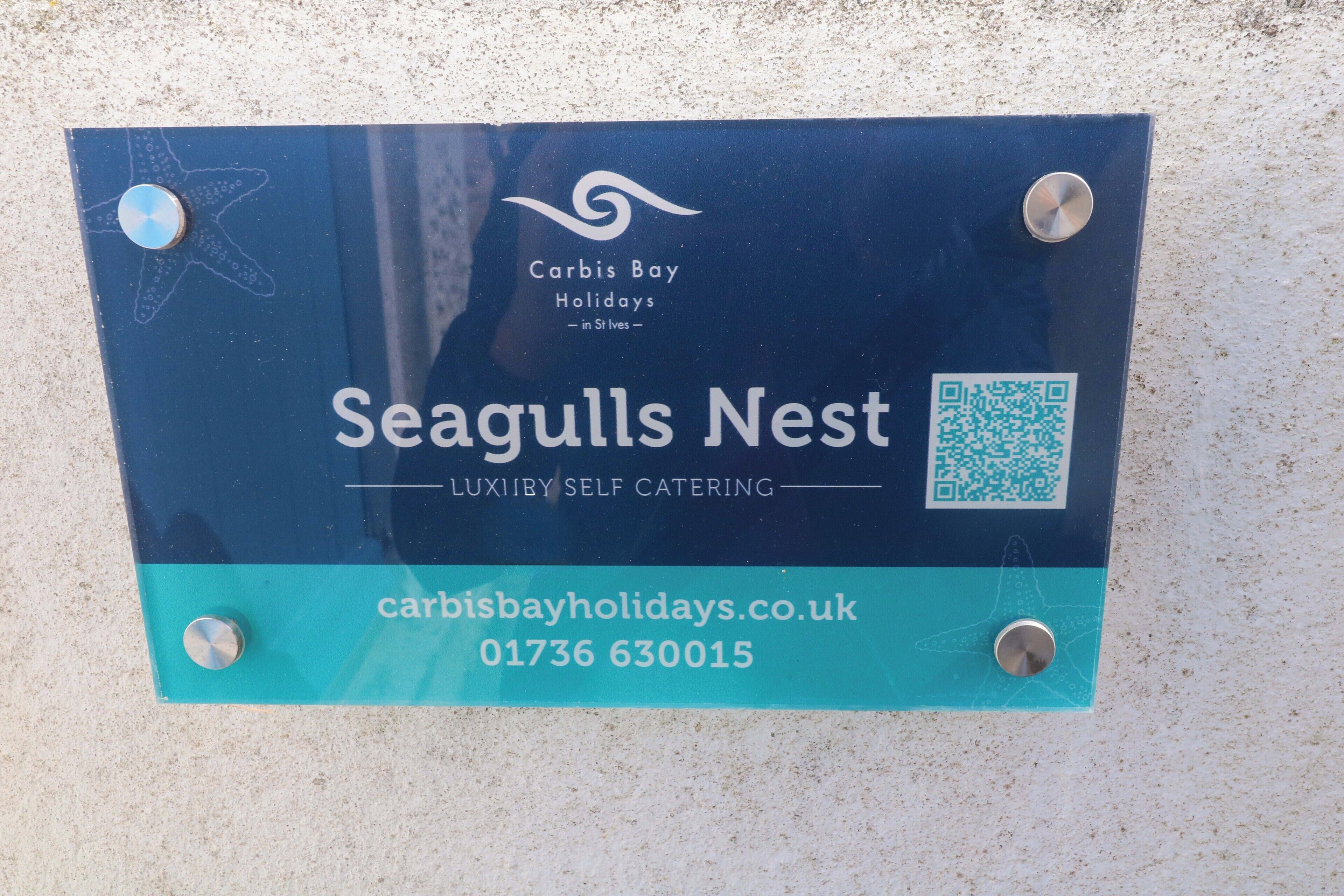 A sign for Seagulls Nest, a luxury self-catering facility at Carbis Bay Holidays, with contact information and a QR code.