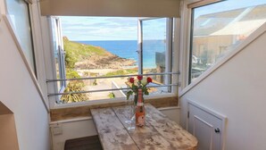 A corner room with a view of the sea, a wooden table with a vase of flowers, and a window sill. - Seagulls Nest (St Ives)
