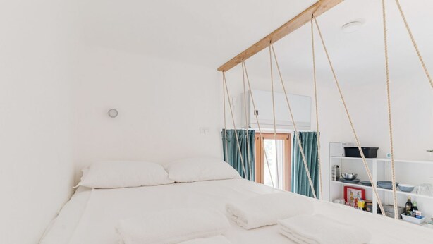 Um quarto branco com uma cama, teto de madeira e uma estante com objetos.