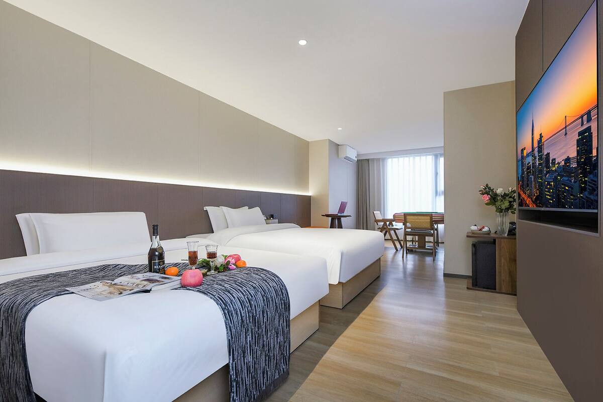 Habitación de hotel con dos camas, un escritorio y un ventanal grande.