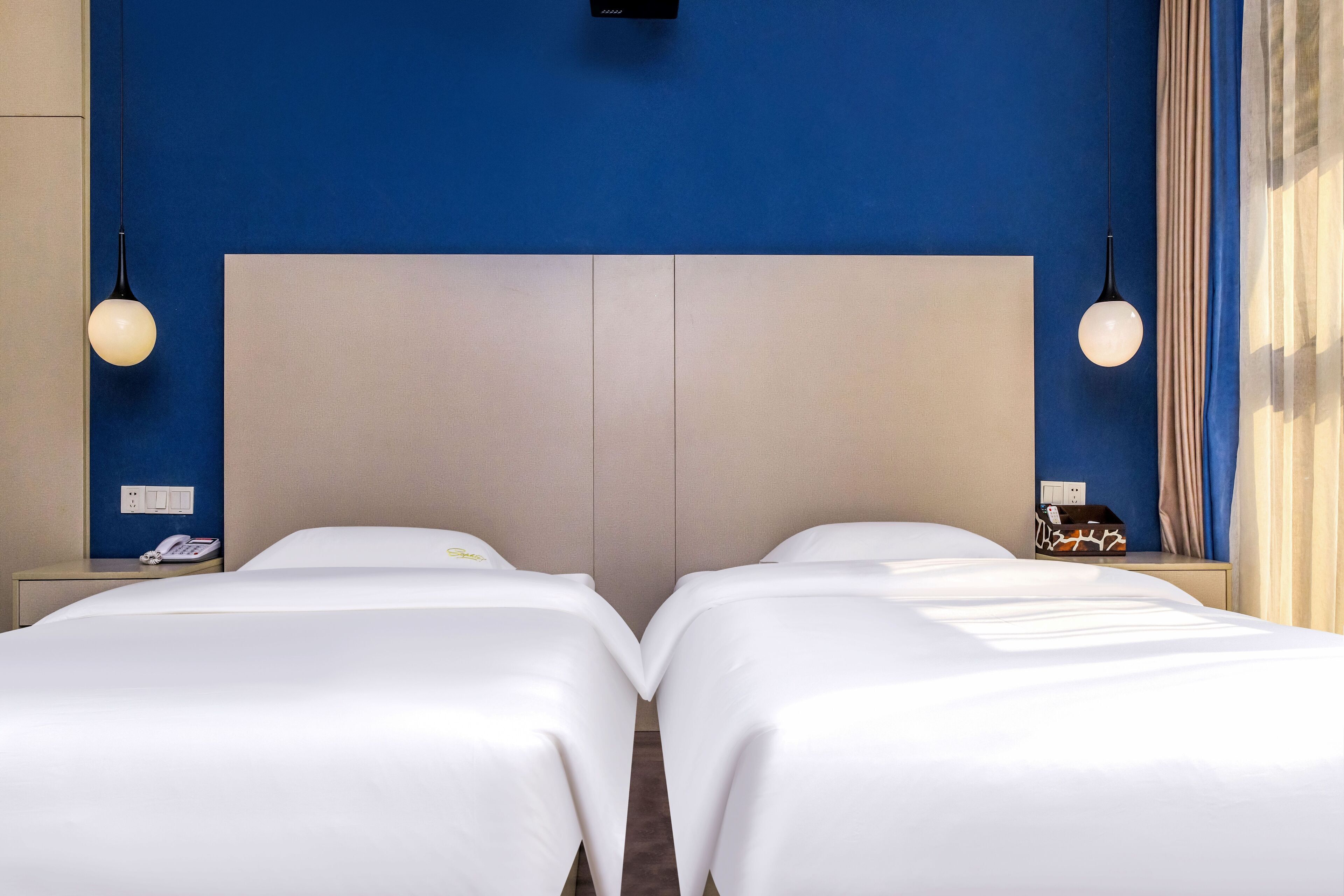 Ein Hotelzimmer mit zwei Betten, einem großen Kopfteil, Nachttischlampen und einem Telefon auf dem Nachttisch.