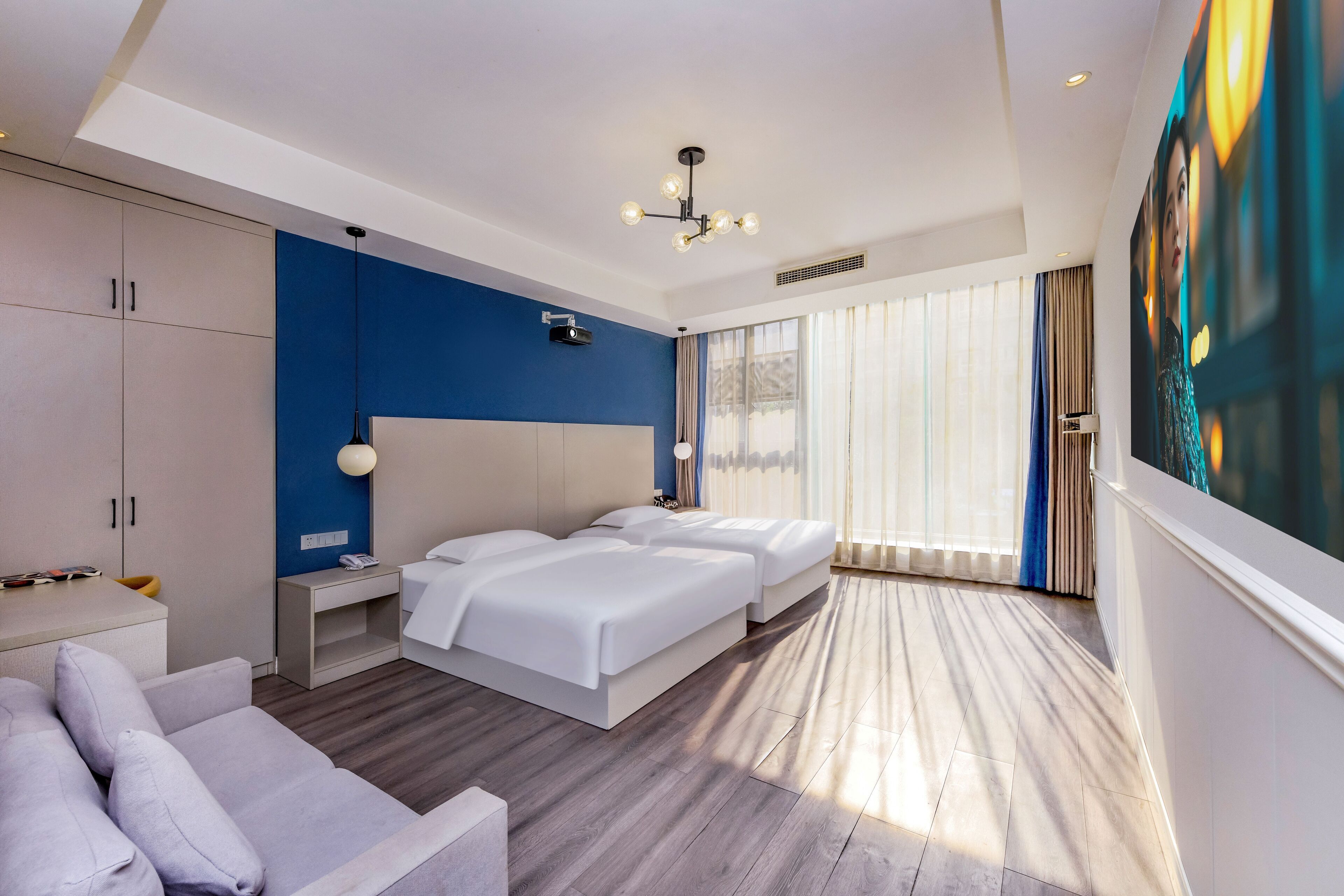 Quarto de hotel moderno com uma cama grande, um sofá, uma escrivaninha e uma janela ampla com cortinas.