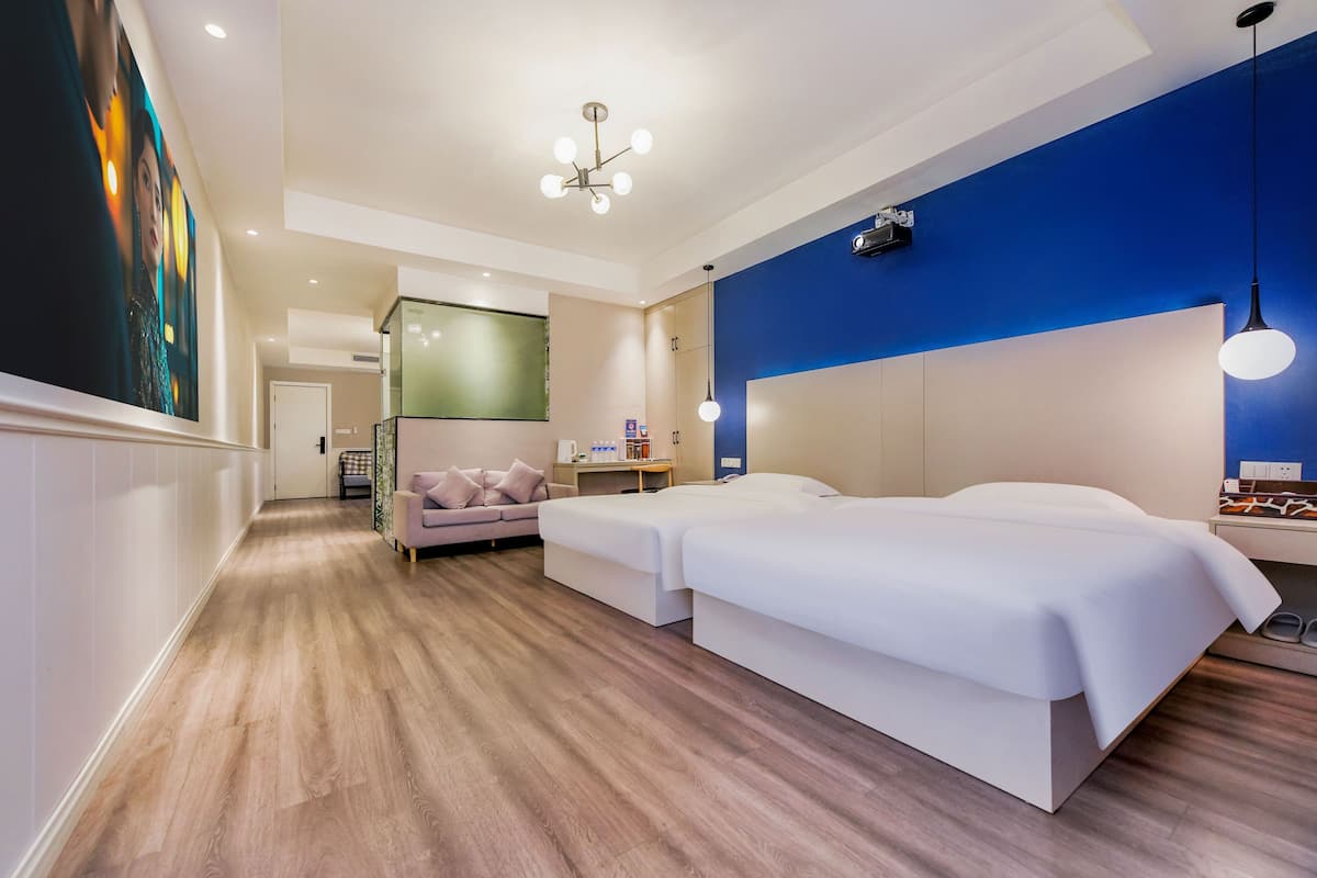 Una habitación de hotel moderna con suelo de madera, dos camas, un sofá, un escritorio y un cuadro grande en la pared.