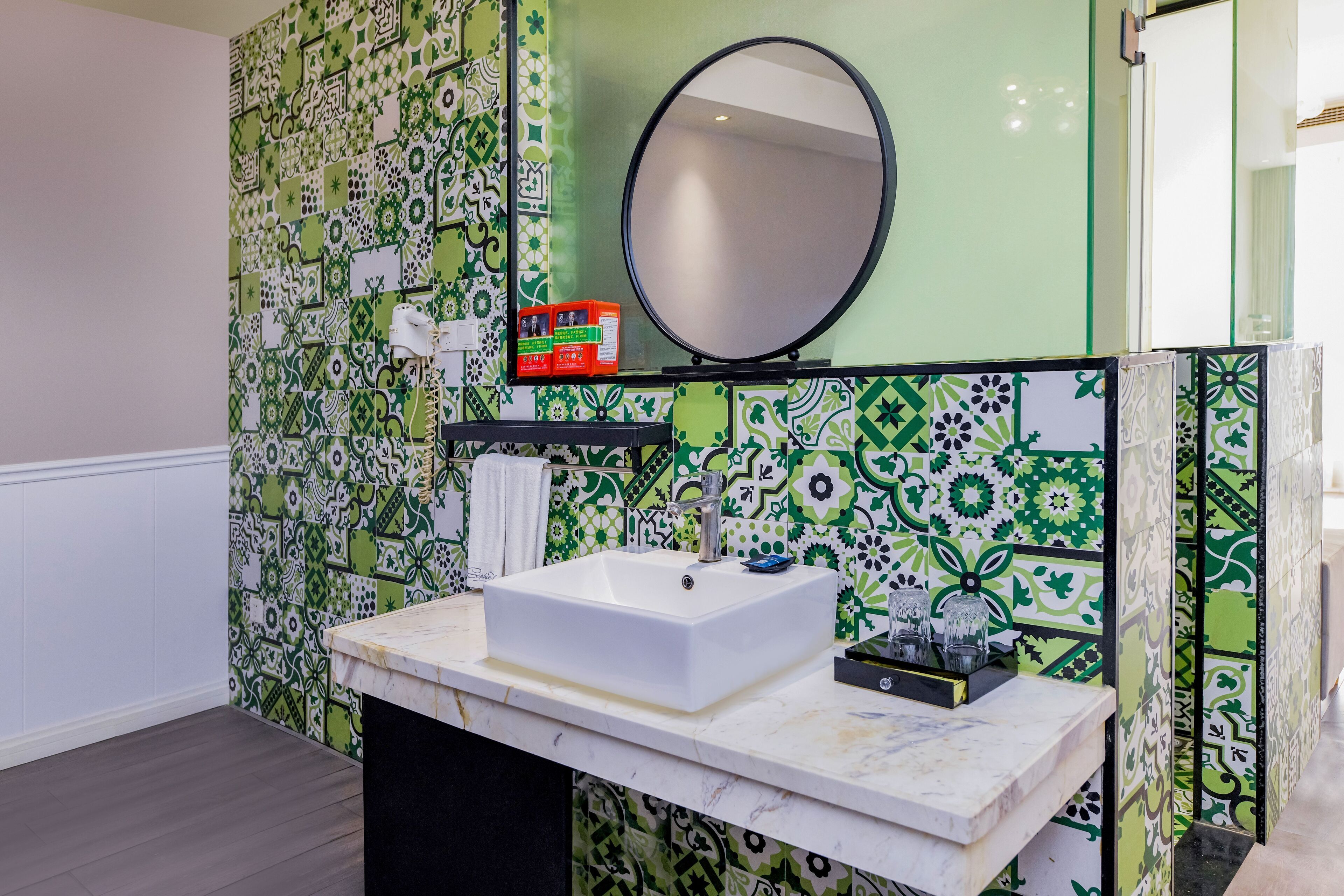 Een badkamer met een witte wastafel, een spiegel en groene en witte tegels met een patroon.