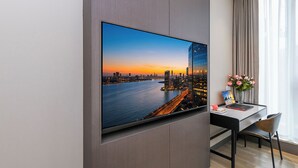 Una habitación de hotel moderna con un televisor de pantalla plana grande montado en la pared, un escritorio con una silla y un jarrón con flores.