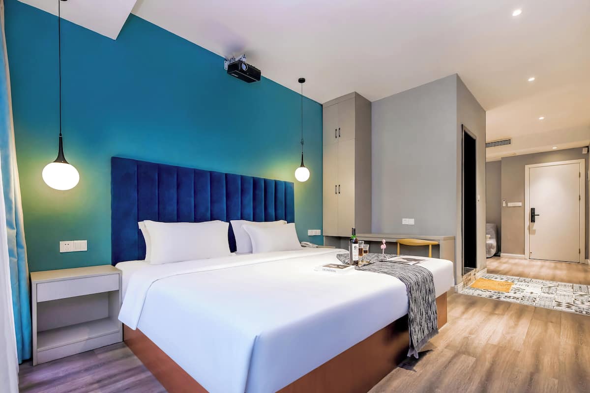 Una habitación de hotel moderna con una cama grande, mesitas de noche, un armario y un baño visible a través de una puerta abierta.