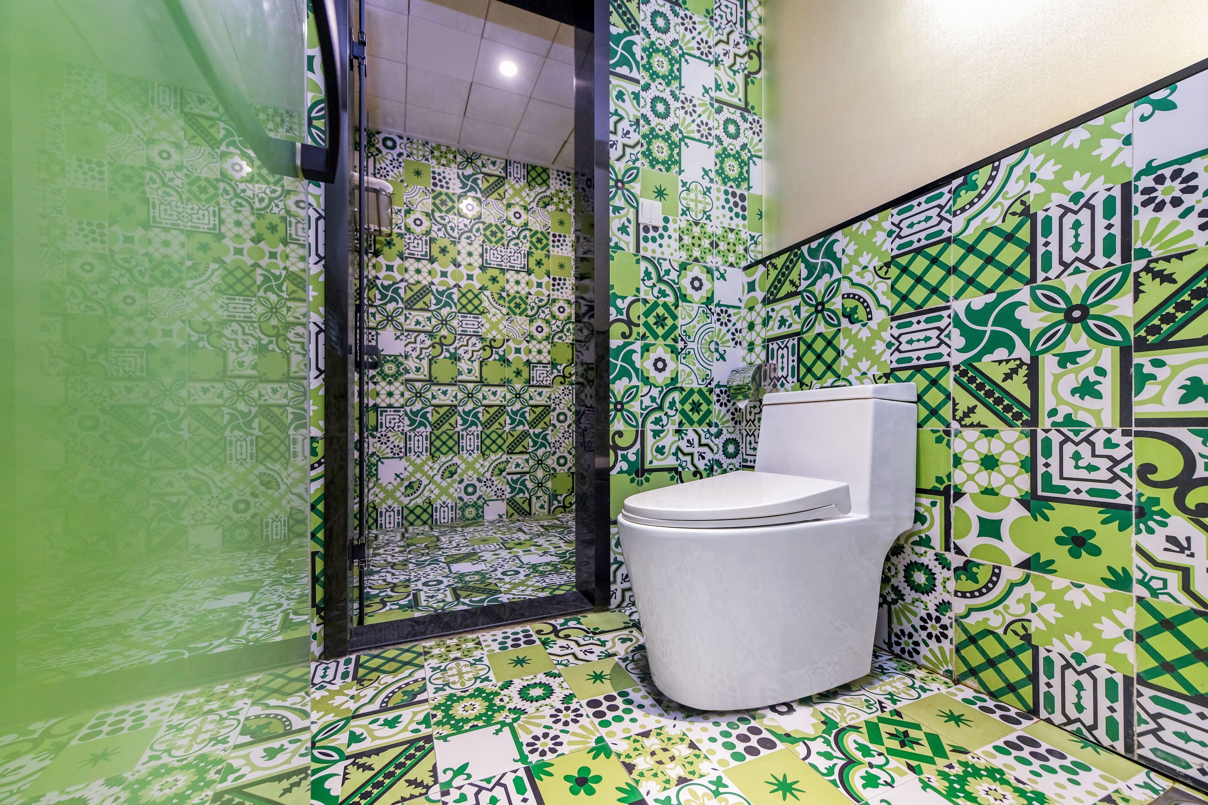 Un baño con un inodoro blanco, baldosas de diseño verde y blanco, y una cabina de ducha de vidrio.