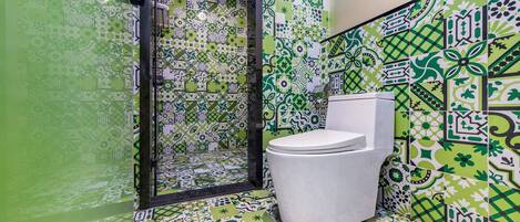 Un baño con un inodoro blanco, baldosas de diseño verde y blanco, y una cabina de ducha de vidrio.