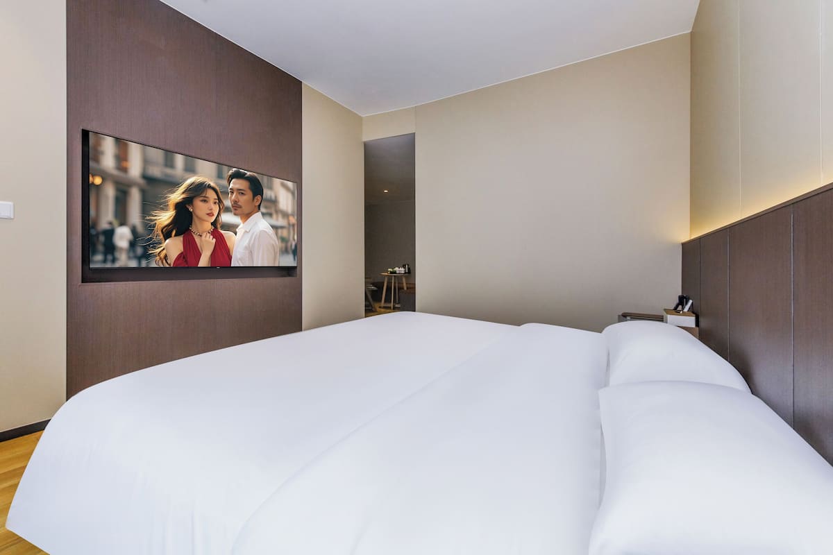 Una habitación de hotel moderna con una cama grande, un televisor de pantalla plana en la pared y un cabecero de madera.