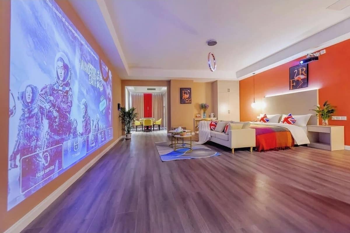 Un vestíbulo de hotel con una pantalla grande mostrando una película, un sofá con banderas británicas y una cortina roja al fondo.