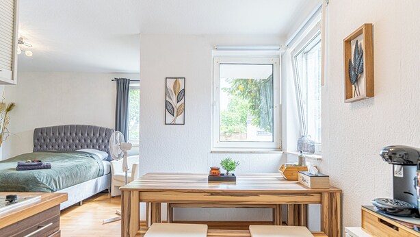 A modern bedroom with a bed, bedside table, and a wooden dining table with benches.
