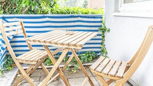 A wooden table and chairs set outdoors, with a striped fabric barrier and greenery in the background.