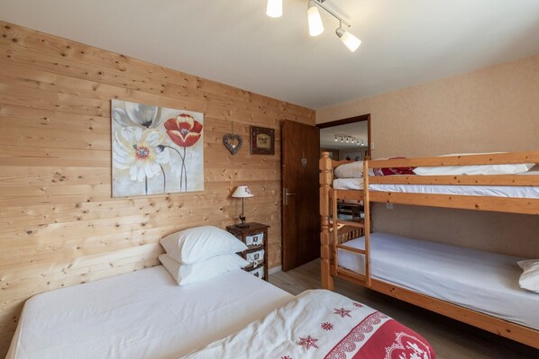 A room with wooden walls, a bunk bed, a single bed, a painting, a lamp, and a small cabinet.