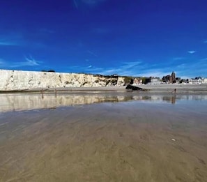 A beach with white cliffs, calm water, and a distant building.