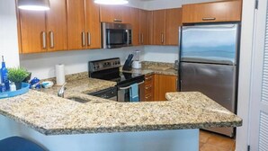 Eine Küche mit Granit-Arbeitsplatten, Holzschränken, Edelstahlgeräten und Pendelleuchten.