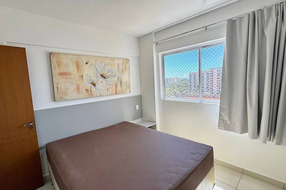 Una habitación con una cama, una ventana con cortinas, una puerta y un cuadro en la pared.