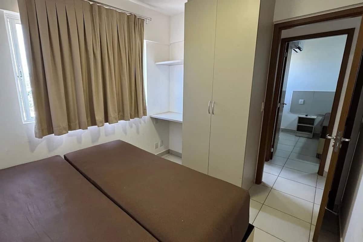 Una habitación con cama, armario, ventana con cortinas y puerta que da a otra estancia.