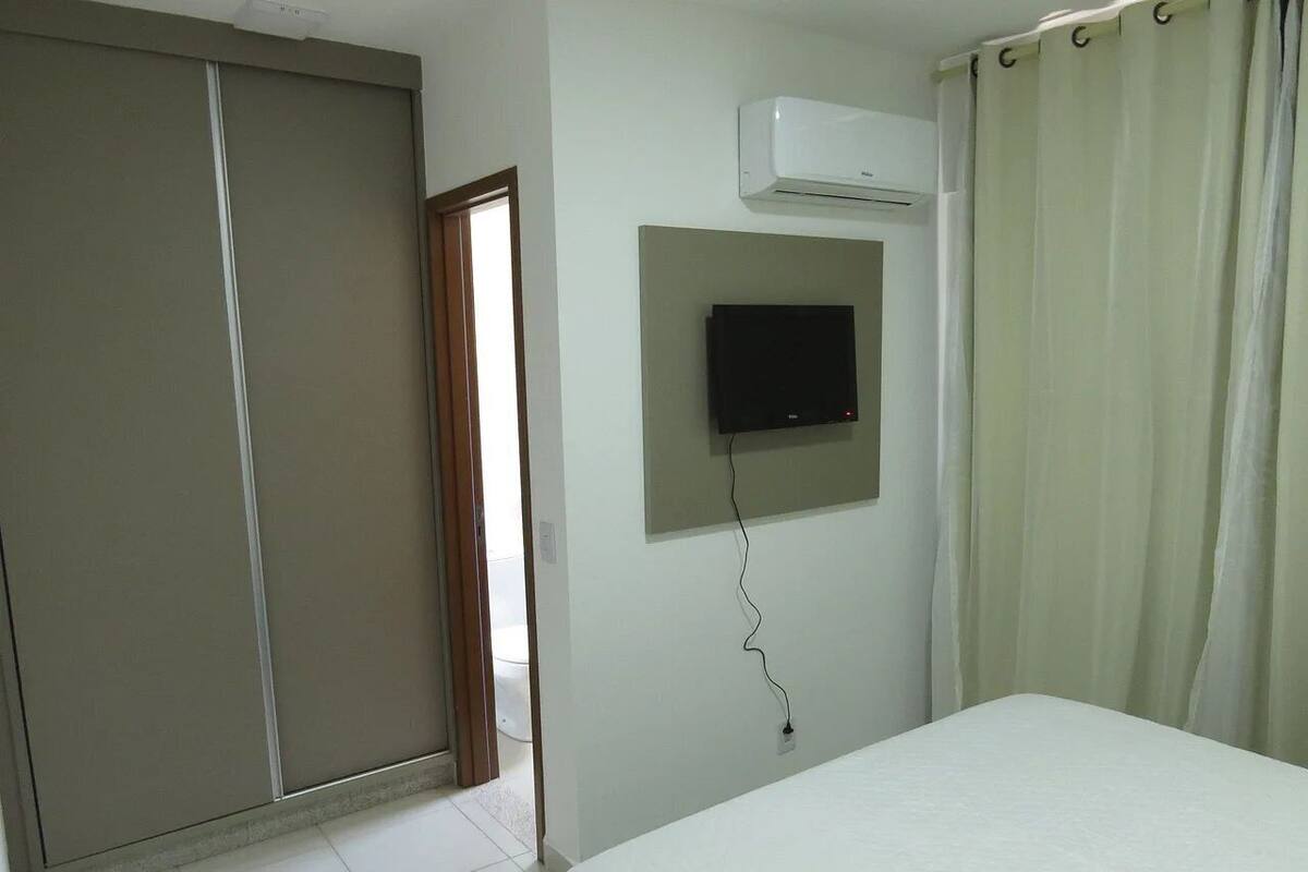 Un dormitorio con cama, televisor montado en la pared, aire acondicionado y una puerta corredera.