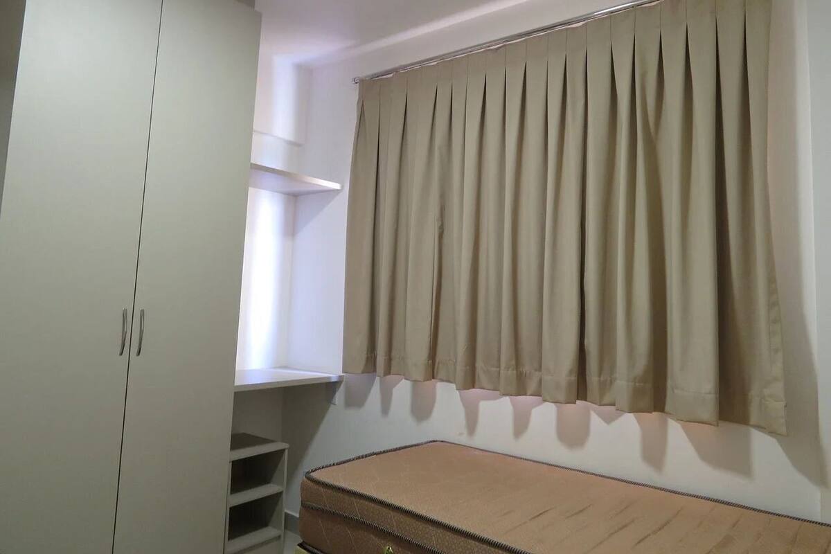 Un dormitorio con cama, armario, ventana con cortinas y estante.