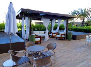 Une terrasse extérieure avec des meubles en osier, un espace salon abrité et un parasol blanc.