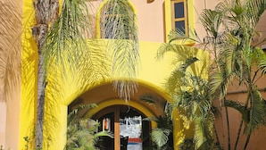 Un bâtiment jaune doté d’une entrée en arc de cercle, entouré de plantes en pot et de palmiers.