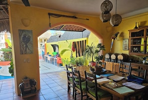 Uma zona de refeições com uma mesa de madeira, cadeiras e vista para a rua através de um arco.