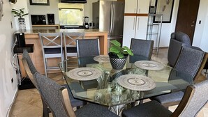 A dining area with a glass table surrounded by chairs, a kitchen in the background, and a potted plant on the table. - Charming, elegant cozy 1-bedroom condo in amazing Tijuana with AC main Blvd SAFE (Tijuana)