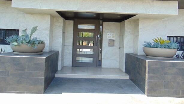 A building entrance with a dark door, two large planters with plants, and a light-colored tiled floor. - Charming, elegant cozy 1-bedroom condo in amazing Tijuana with AC main Blvd SAFE (Tijuana)