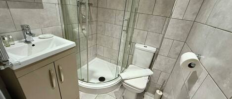 Un baño compacto con cabina de ducha de vidrio, un lavabo blanco y un inodoro.