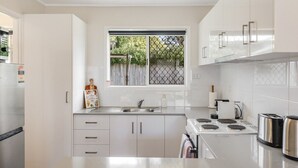 Una cocina moderna con armarios blancos, un refrigerador de acero inoxidable, una ventana con vista a vegetación y una estufa integrada.