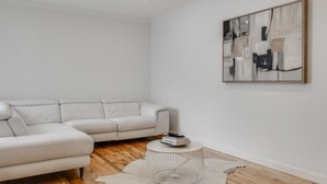Una sala de estar moderna con un sofá seccional blanco, una mesa redonda de centro y un cuadro abstracto grande en la pared.