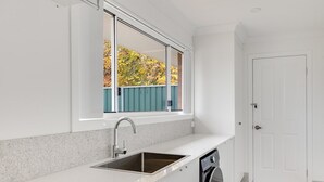 Cocina moderna con lavavajillas integrado, ventana con vistas a árboles y una puerta blanca.