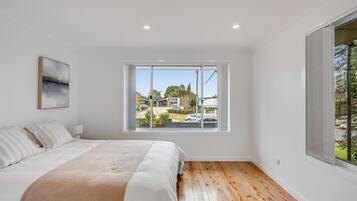 A bedroom with a large window, a bed with white bedding, and a wooden floor.