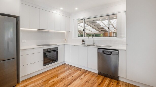 Una cocina moderna con armarios blancos, electrodomésticos de acero inoxidable y piso de madera.