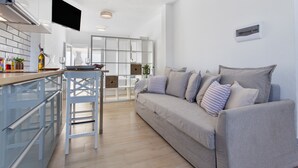 Una cocina moderna con un televisor de pantalla plana, una barra, un sofá gris y una zona de comedor con mesa y sillas blancas.