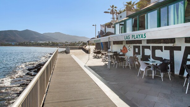 Un restaurante frente al mar con terraza, vistas al océano y montañas al fondo.
