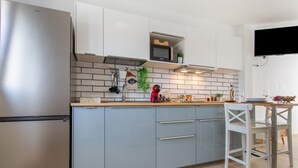 Una cocina moderna con un refrigerador de acero inoxidable, gabinetes grises, un microondas y un comedor con una mesa y sillas blancas.