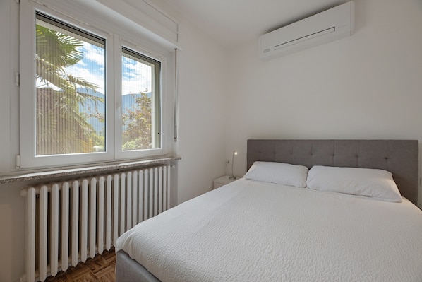 Un dormitorio con cama, ventana, radiador y unidad de aire acondicionado.