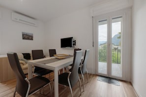 Un comedor moderno con una mesa, sillas, un televisor y vistas a un balcón.
