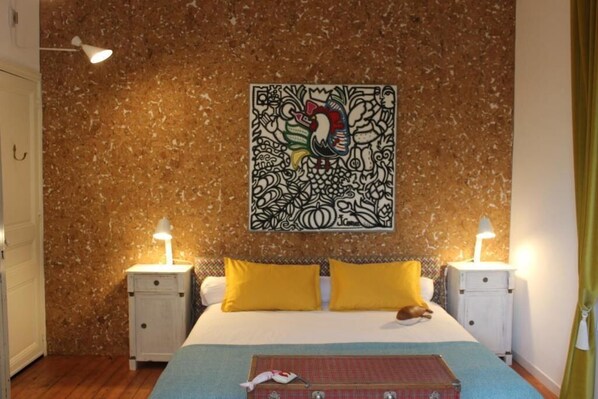 A bedroom with a bed, two bedside tables, yellow pillows, a wall tapestry, and a nightstand lamp.