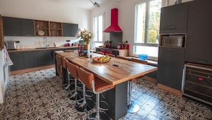 A modern kitchen with a central island, bar stools, a red hood, and a patterned floor. - Villa Kumquats (Béziers)