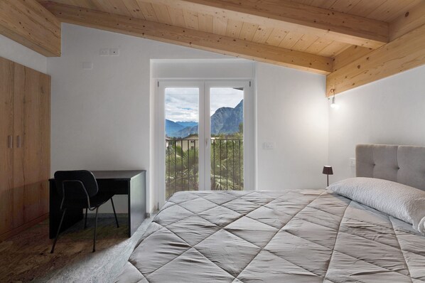 Une chambre à coucher avec un lit, un bureau et une chaise. On peut voir des montagnes à travers la porte.