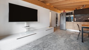 Een moderne keuken met een groot flatscreen televisietoestel, houten balken in het plafond en een marmeren vloer.