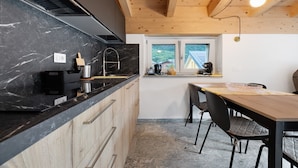 Een keuken met een marmeren aanrechtblad, houten keukenkastjes, een zwart fornuis en een eethoek met een tafel en stoelen.