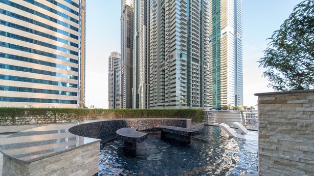 A modern outdoor pool area with geometric stone seating and a clear view of high-rise buildings in the background. - Magnificent 2BR at Dubai Marina (Dubai)