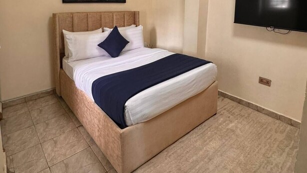 A hotel room with a bed, a painting, a television, and a tiled floor.
